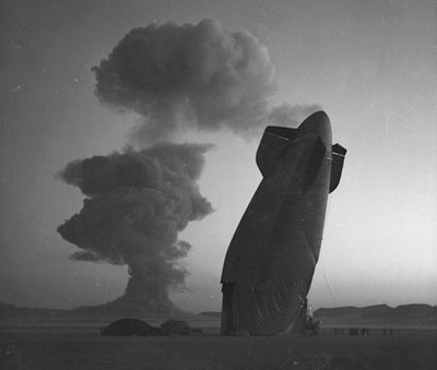 The tail section of a U.S. Navy Blimp is shown with the Stokes cloud in background at the Nevada test Site on August 7, 1957. The airship was unmanned and was used in a military effects experiment.